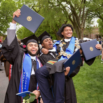 A group of three graduates celebrating joyously, one of them lifting the other up in their arms.
