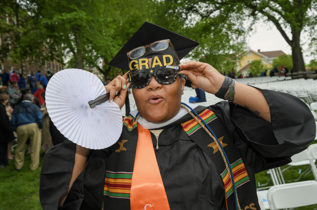 A graduate poses for a silly photo, holding up their sunglasses.