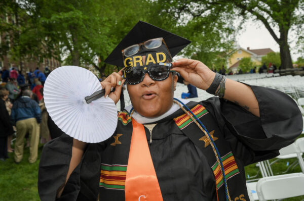 A graduate poses for a silly photo, holding up their sunglasses.