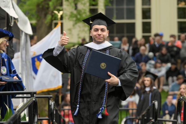 A graduate proudly shows off their diploma, giving the crowd a thumbs up.