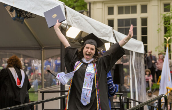 A graduate lifting their arms in the air triumphantly after receiving their diploma.