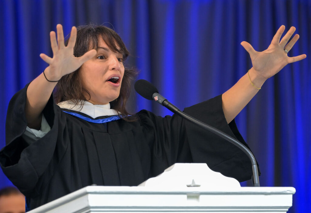 Honorary Degree recipient, Mónica Guzmán, gives a passionate speech, her hands raised.