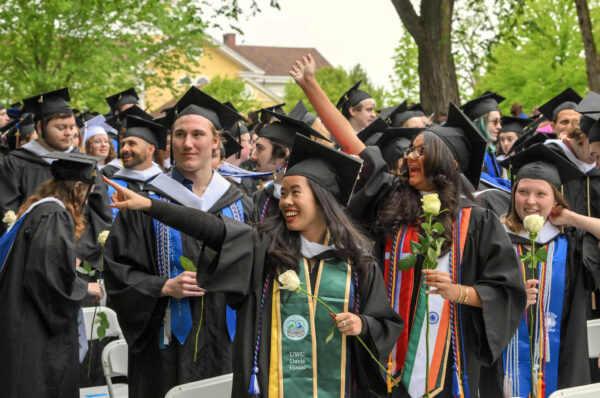 Graduates smile and point at something off-camera during the commencement ceremony.
