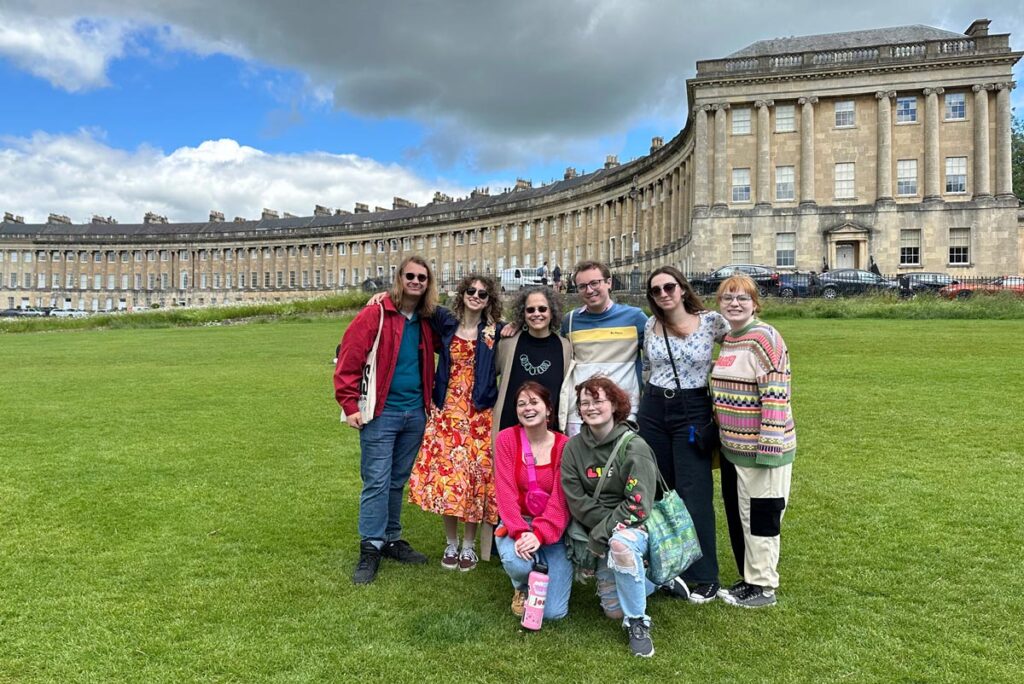 Eight individuals gather on the lawn in front of a crescent architectural building in Bath, England.