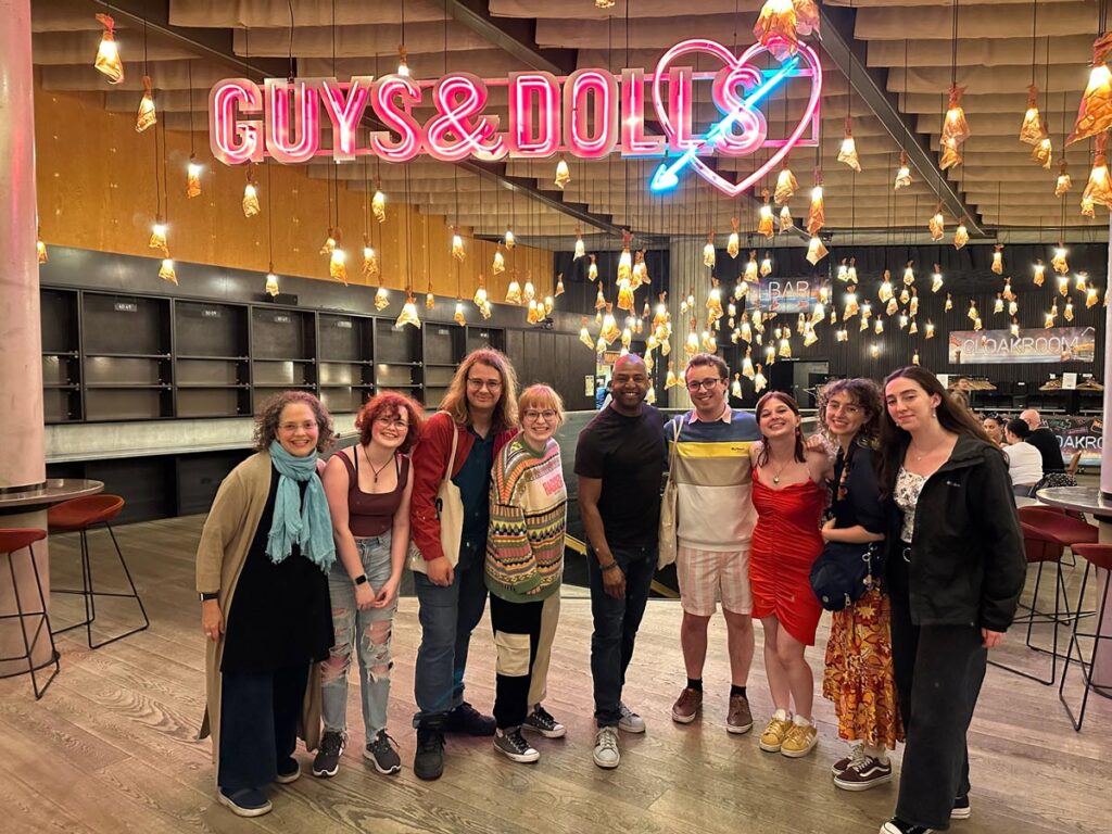 Nine individuals smile at a gathering after a performance of Guys and Dolls.