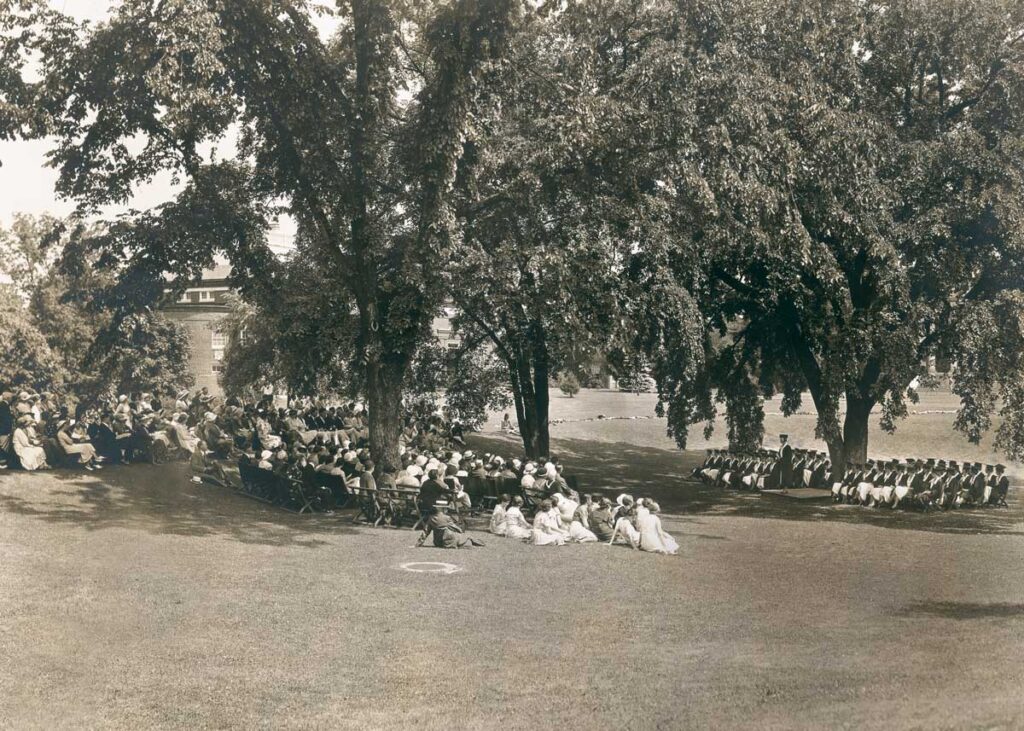 Students and audience face each other on the Dimple during a commencement ceremony under the trees in 1932
