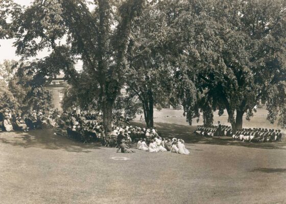 Students and audience face each other on the Dimple during a commencement ceremony under the trees in 1932