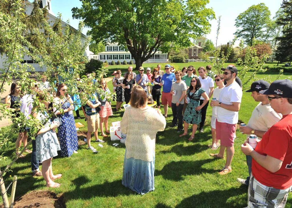 A group of young people gather on a lawn among a growing orchard of apple trees.